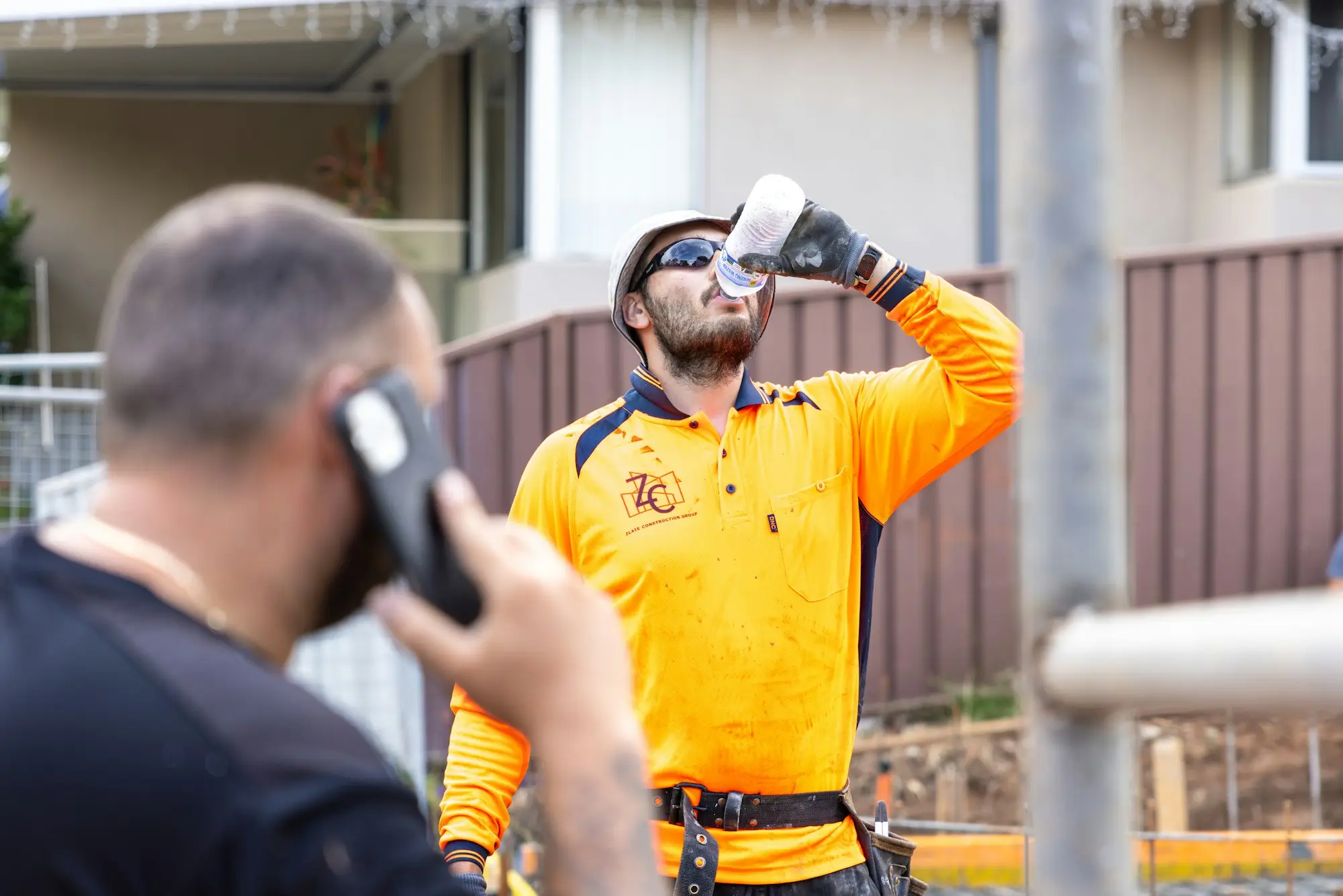 Tradie in hi-vis taking a break on site while a colleague makes a phone call