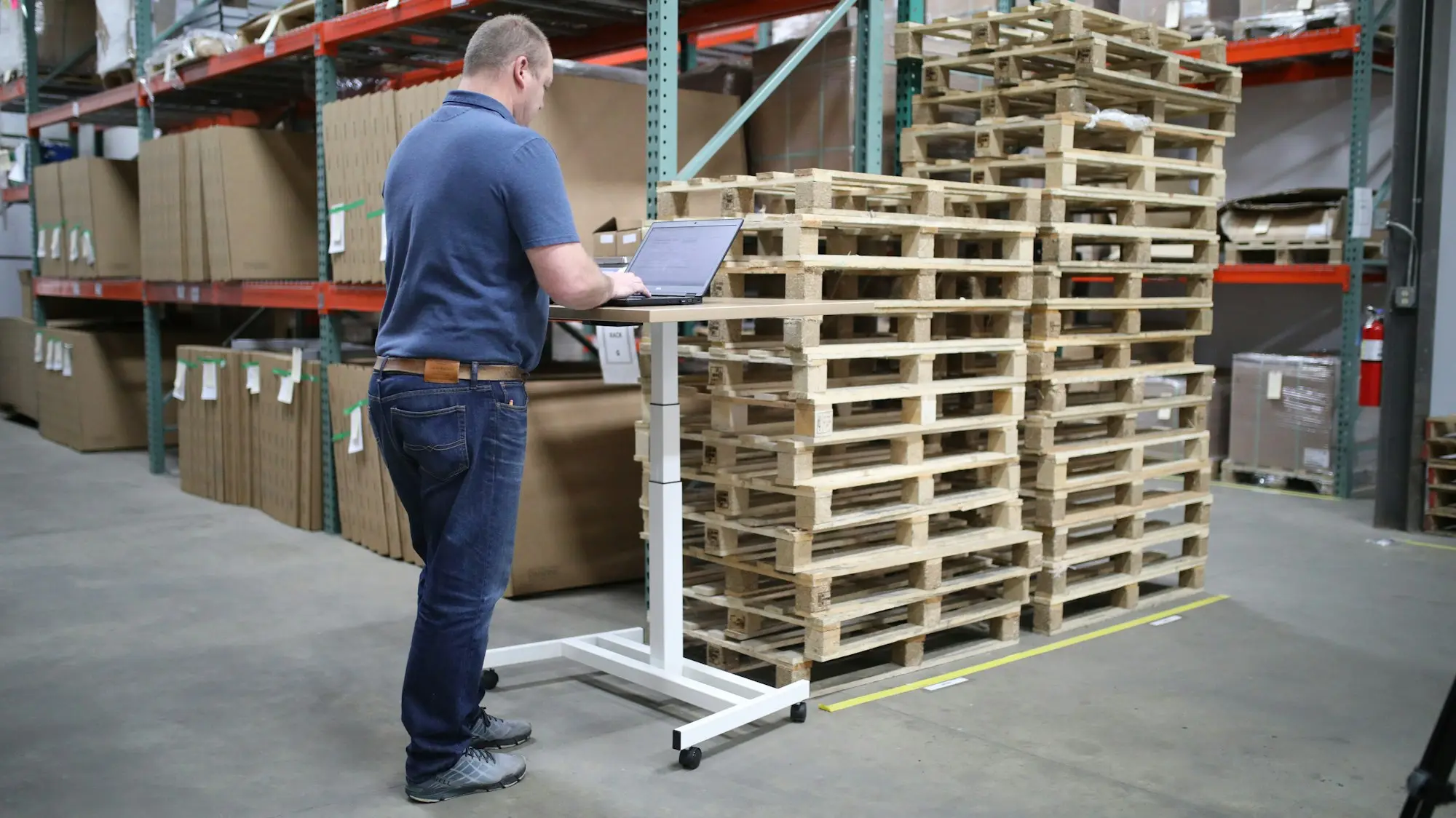 Warehouse manager working at a mobile laptop stand beside stacked pallets